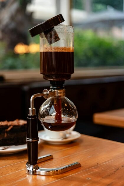A siphon coffee brewer filled with dark coffee on a wooden cafe table