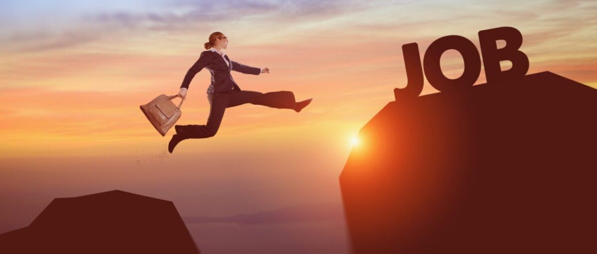 A person in a suit leaping toward the word JOB at sunset
